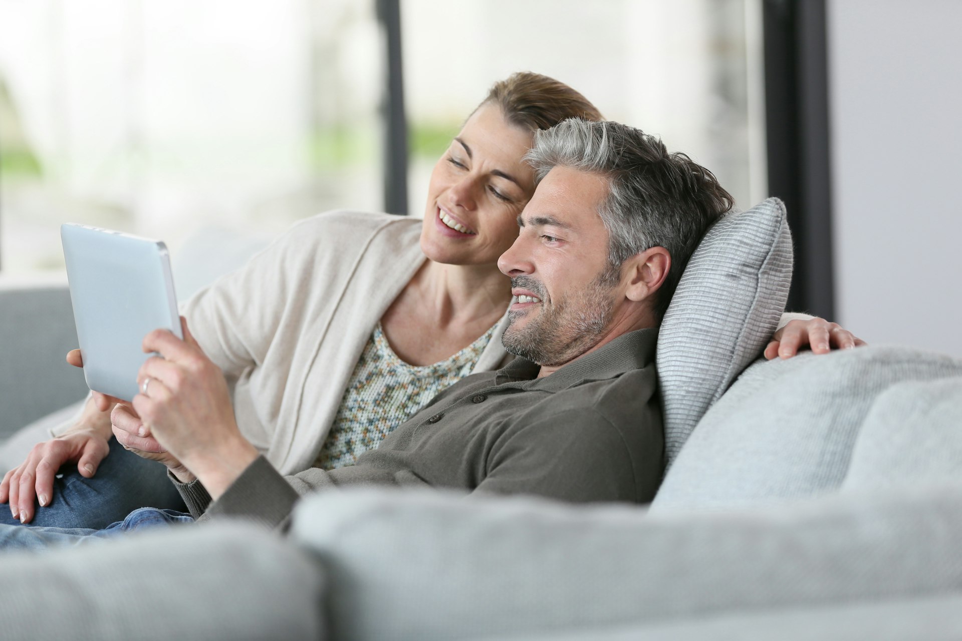 Landlords relaxing on the sofa smiling, while checking their property online
