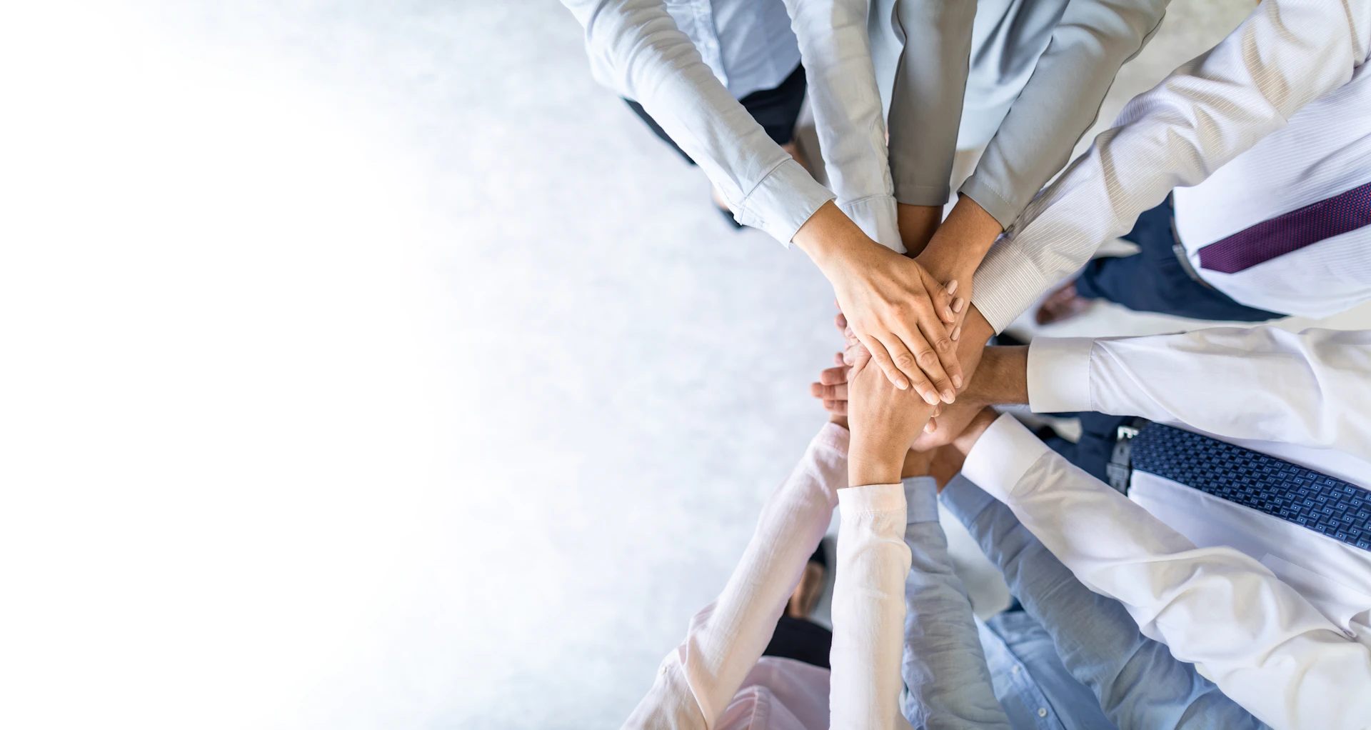 Team of employees putting their hands together in the center of a circle to show teamwork